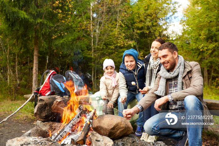 camping, travel, tourism, hike and people concept - happy family roasting marshmallow over campfire