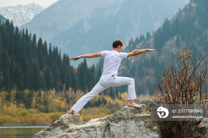 A man practices yoga on a background of mountains. Pose Virabhadrasana 2 or warrior