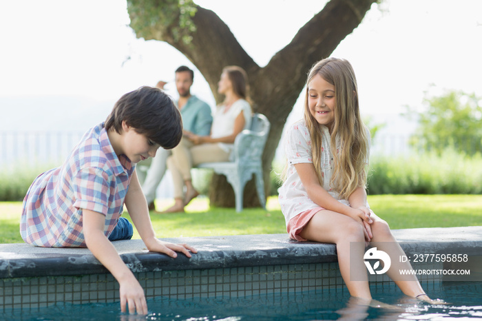 Brother and sister playing at edge of swimming pool