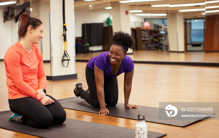 Female athletes talking while kneeling on exercise mats in yoga class