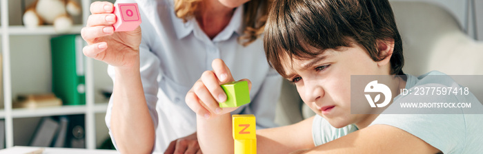 panoramic shot of kid with dyslexia and child psychologist playing with building blocks