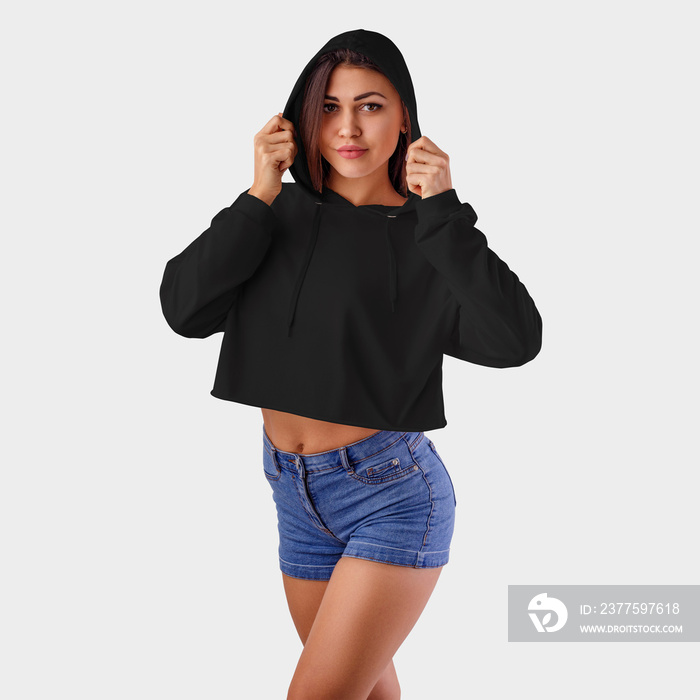 Mockup of a black female crop top on a pretty girl in blue shorts, wearing a hood, in the background