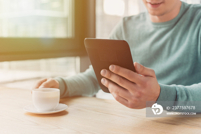 cropped view of man studying with ebook and holding cup of tea at home