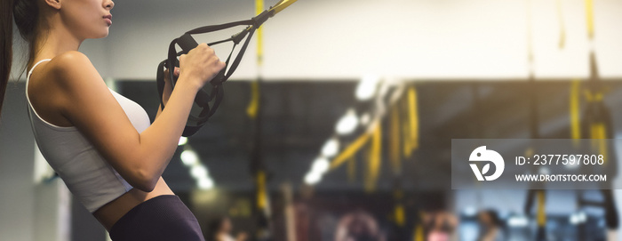 Woman exercising with suspension trainer in gym, copy space