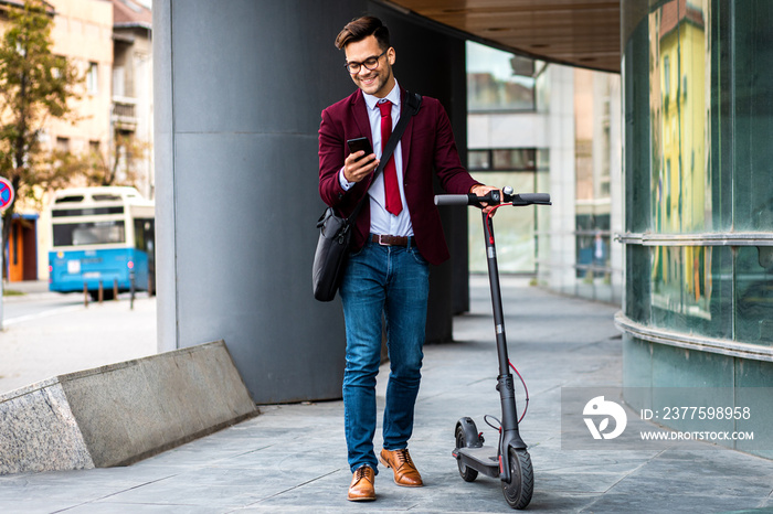 Smiling businessman with electric scooter standing in front of modern business building looking at p