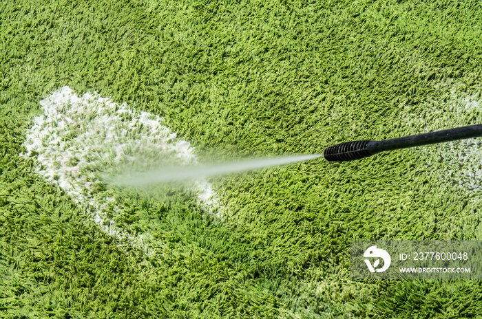 Carpet washing. Cleaning a green large hairy rug with a large jet of water