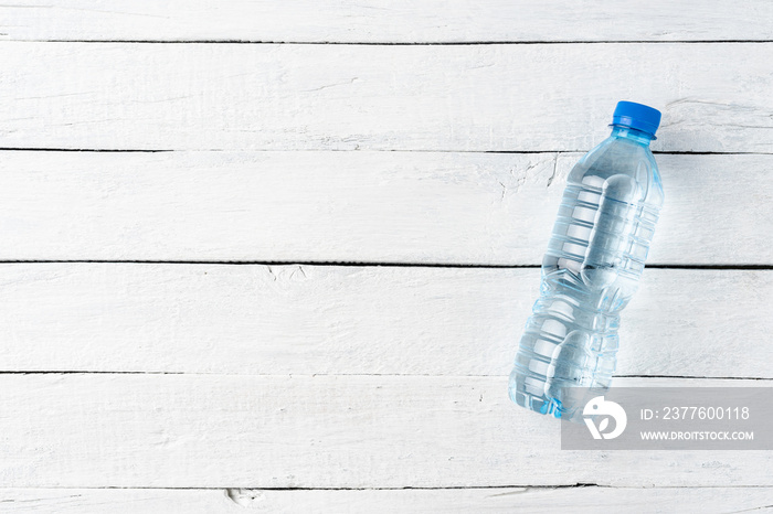 Overhead shot of mineral water in small plastic bottle on white wooden background with copyspace