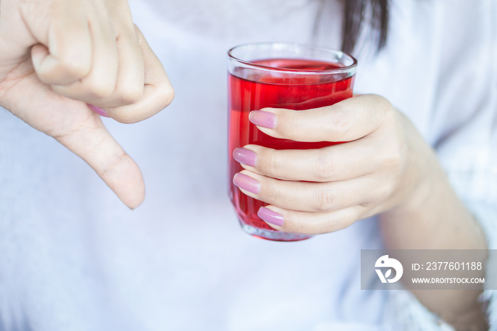 woman hand holding glass of red soda with hand thumbs down ,unhealthy drinking and sugar addiction concept background