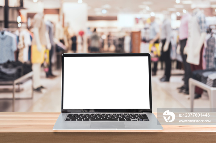 Empty screen laptop on a wooden table with abstract blurred background of interior clothing store at Shopping Mall