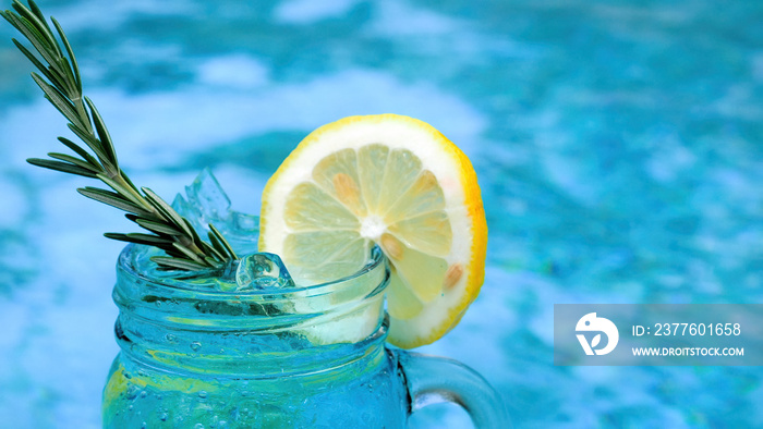 Non-alcoholic blue cocktail with rosemary and lemon slice near swimming pool. Summer tropical bar at hot sunny day. Relax poolside, refreshment drink. Vacation at luxury hotel in heat