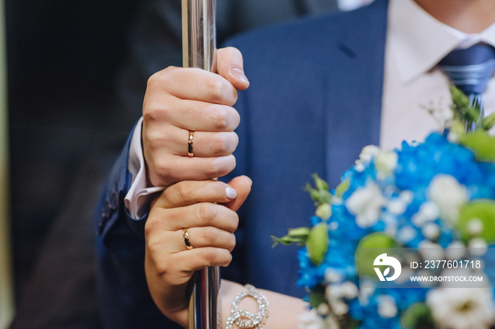 Hands of the newlyweds with golden rings close-up. The bride and groom stand in a bus, tram and hold on to a metal handrail. Photography, concept.