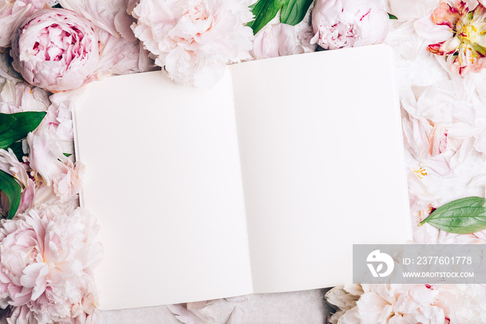 Frame made of pink peony flowers and open notebook for writing your dreams or manifistations. Feminine flower composition. Flat lay, top view.