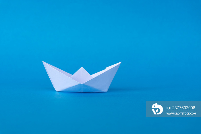 Business concept - paper ship origami on blue background.