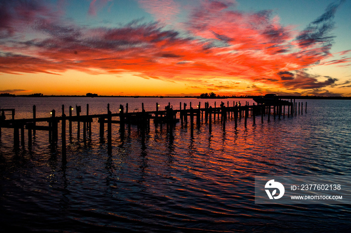 A flaming orange sunset reflecting in the bay and the silhouette of a pier in Dunedin, Florida.