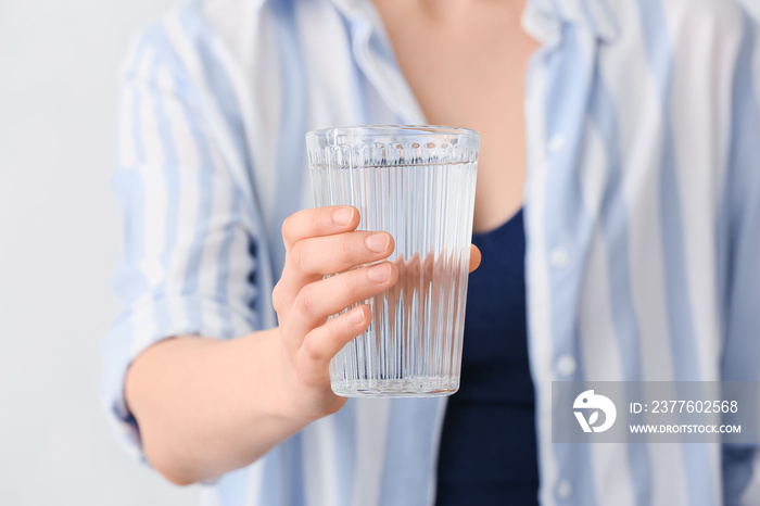 Woman holding glass of water on light background