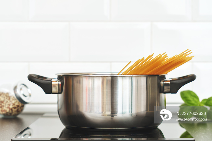 Home kitchen. Cooking food for lunch. Saucepan with spaghetti on the hob. Leaves of basil and seasoning. Background for your text and design