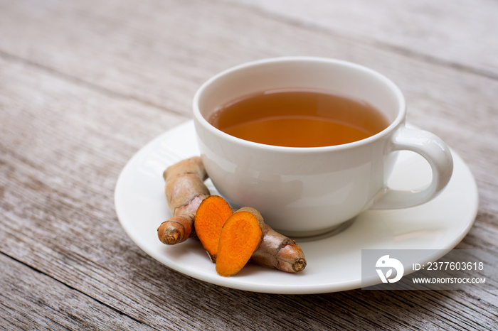 Closeup cup of hot Turmeric tea with tumeric root isolated on wood table background .