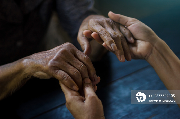 The daughter  holding hand and takes care mother elderly that is alzheimer and parkinson’s patient on dark background.