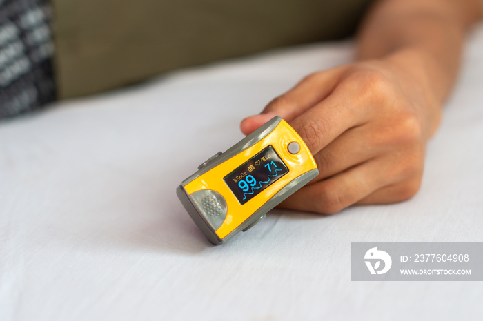 Close-up of woman’s hand resting on bed, wearing pulse oximeter to measure blood oxygen saturation