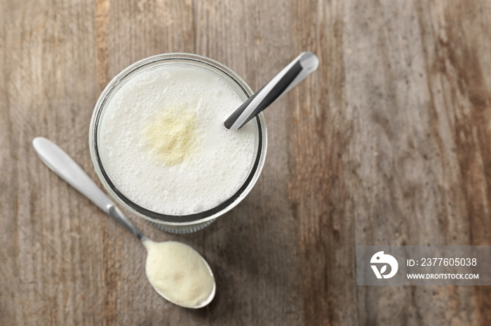 Glass with protein shake and powder in spoon on wooden table