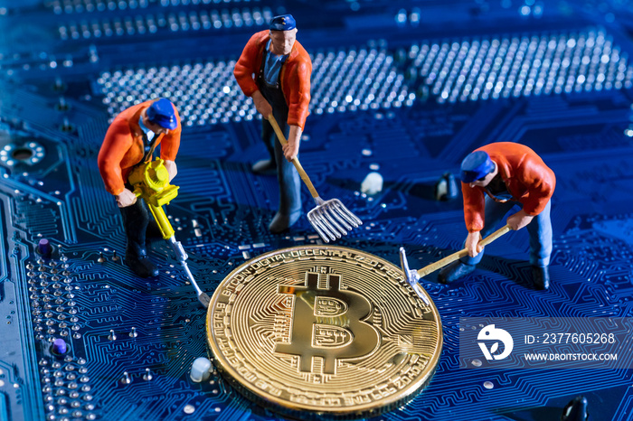 Bitcoin mining miniature worker, small figure holding mattock digging on shiny golden Bitcoin crypto currency coin on electronics cyber look blue circuit board with soldering.