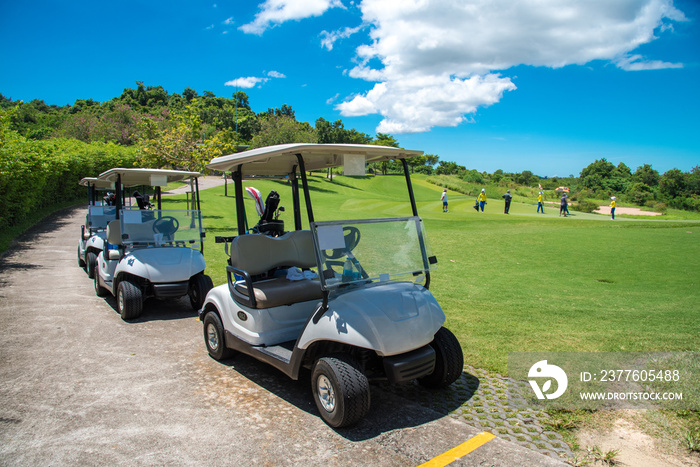 Golf carts parking near golf course with golfers and caddie are in competition,blue cloud sky background.