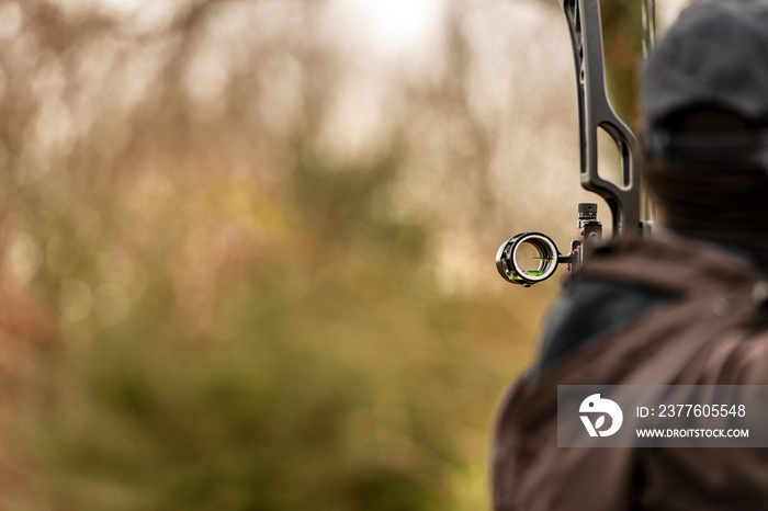 Close-up of an archer, back view, while aiming with a hunting compound bow, with blurred vegetation in the background