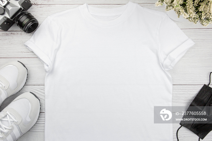 White womens cotton t-shirt mockup with sneaker, retro camera and face mask on white wooden background. Design t shirt template, print presentation mock up. Top view flat lay.