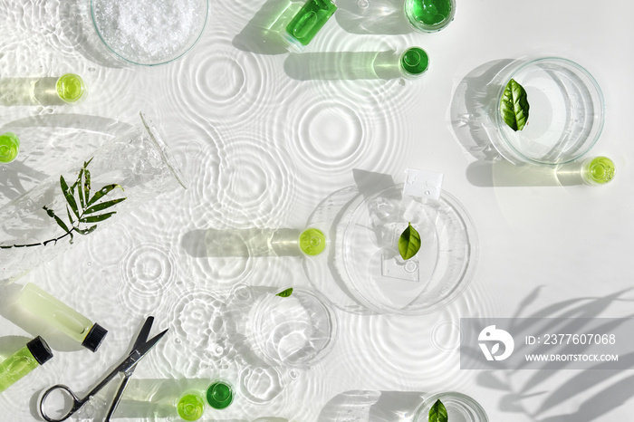 Cosmetic skincare background. Herbal medicine with green leaves. Natural sunlight, long shadows. Splashes of water, ring shadows . Chemical glassware, petri dishes, vials. Natural skincare concept.