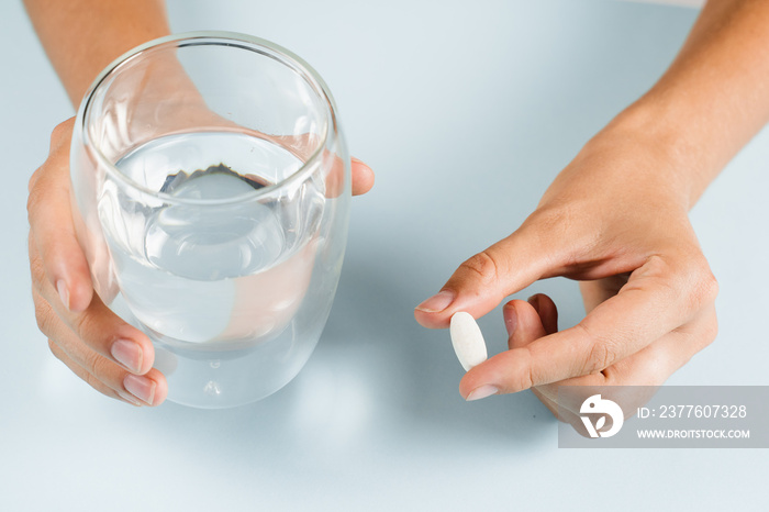 White pill of dietary biologically active supplements and glass of water for daily tablets intake on blue background.