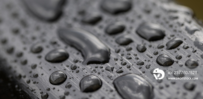 drops of water on dark water-repellent surface close-up as background for design with short focus. Beautiful abstract background of water drops on black. Non-wetting coating, water-repellent layer