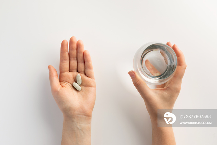 Hands holding a glass of water and pills. Top view.