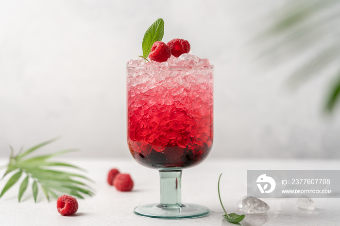 Glass of bright pink raspberry drink with crushed ice on light background. Refreshing berry summer drink