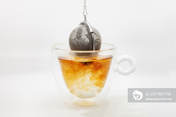 Tea strainer with tea leaves dropped in glass cup of boiling water