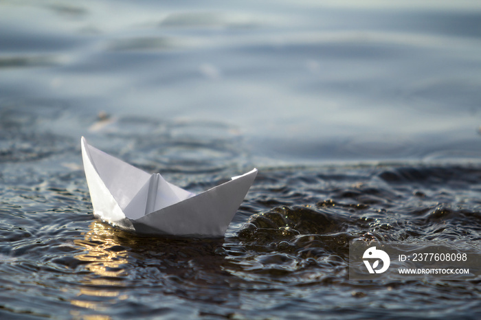 Close-up of simple small white origami paper boat floating in blue clear river or sea water under bright summer sky. Beauty of nature, freedom, dreams and fantasies concept.