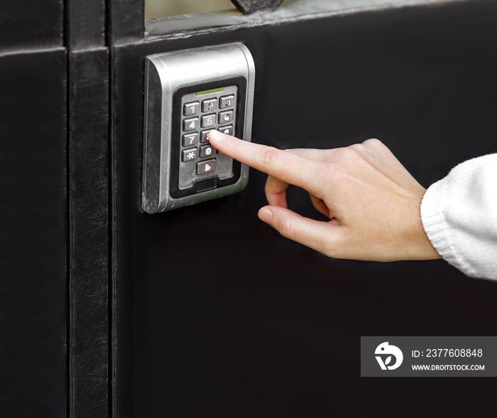 female hand dials the access code on the electronic lock by pressing a index finger on button, closeup of the security lock on black iron gate with copy space.