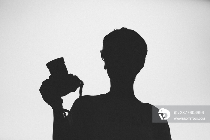 Silhouette portrait of woman holding a camera in the hand.