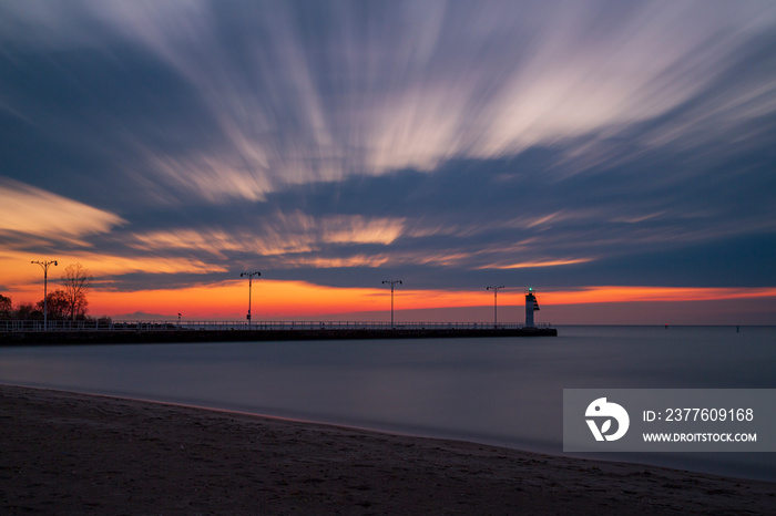 An early morning sunrise breaks through the fast-moving clouds as a lighthouse sits on the banks of Lake Ontario