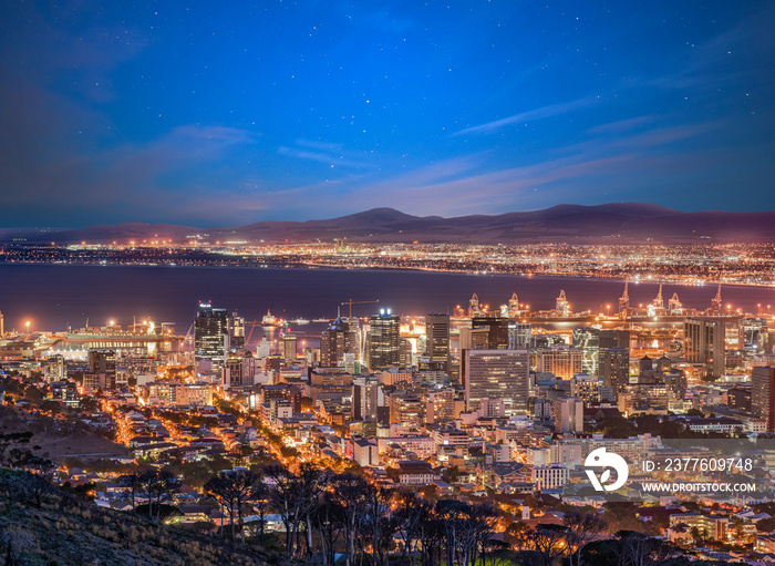 Cape Town city and harbour illuminated at night with stars and moving clouds in the sky