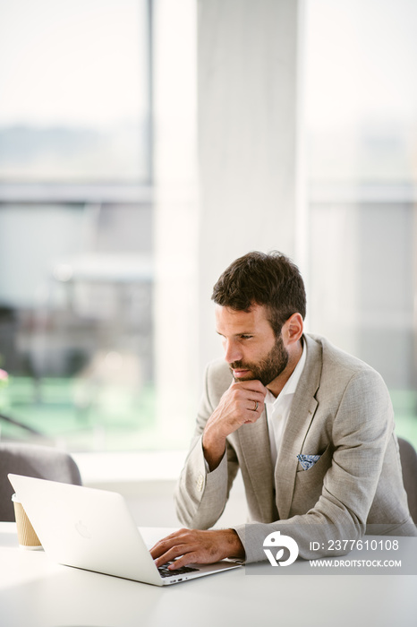 Businessman sitting looking at his laptop. Businessman working in the office on his laptop. Stylish businessman working on a project in the office thinking about future