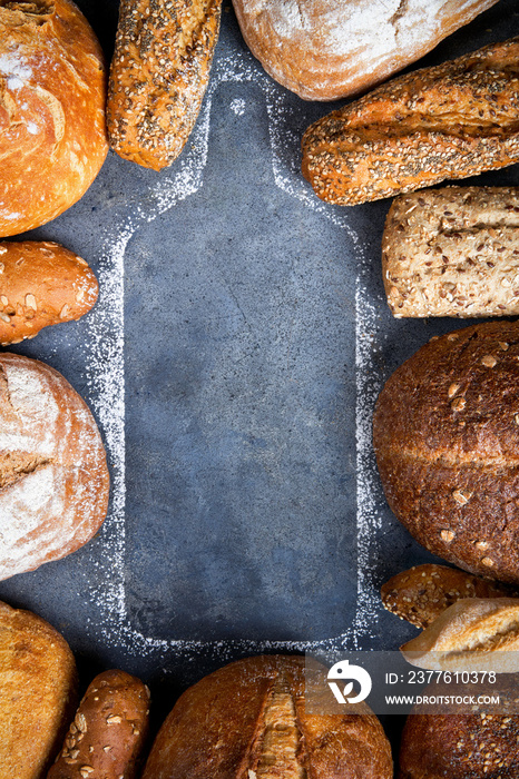 A variety of breads surrounded by a silhouette wooden cutting board on a gray surface, top view, copy space. Food bakery shop concept background.