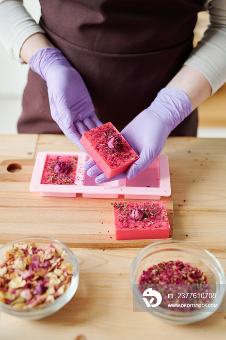 Hands of young woman in lilac gloves holding bar of fresh handmade floral soap