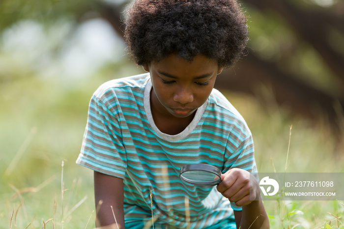 Child boy exploring nature with magnifying glass outdoor. Education, field trips, researcher and discovery concept