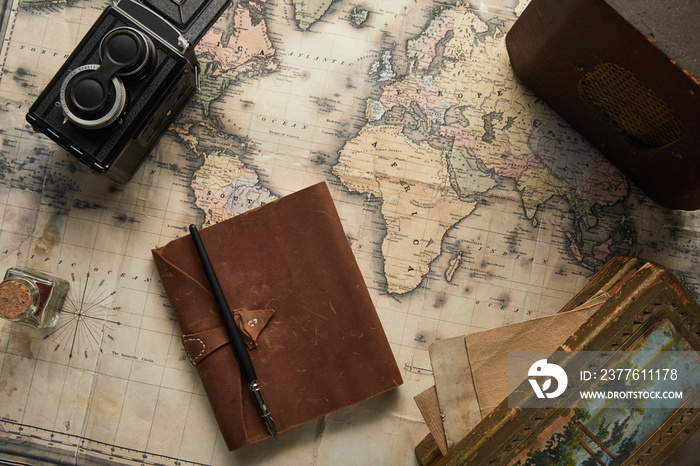 top view of vintage camera, notepad with fountain pen, radio and painting on map background