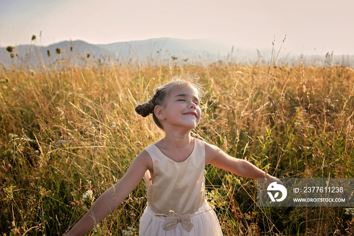 Cute girl dancing through a beautiful meadow with wheat and flowers in the mountains