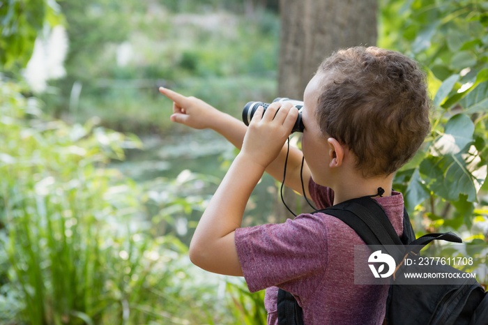 Boy looking through binoculars and pointing in the forest