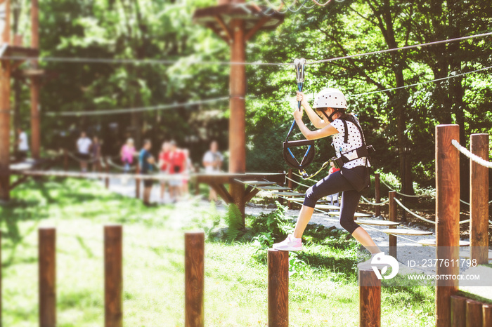 Brave little girl in the forest adventure park, wearing helmet and safety equipment at amusement center for children outdoor