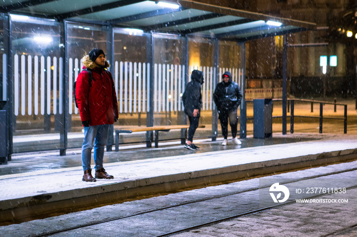 man at winter snowed night at railway station waiting for tram