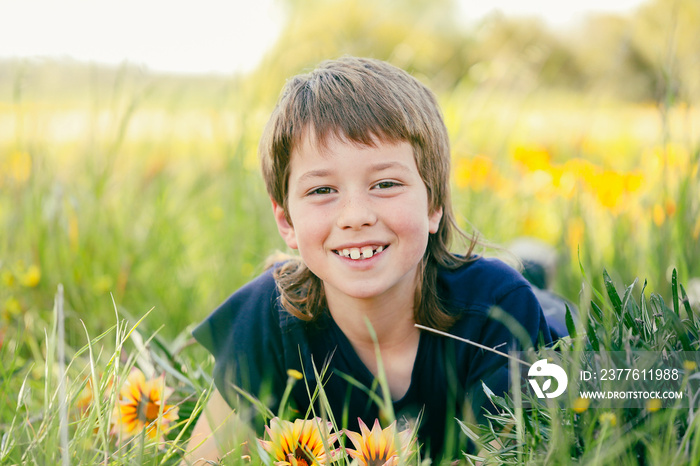 Boy with mullet hairstyle lying in long grass with wildflowers