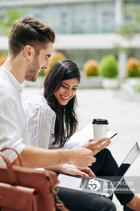 Happy young businessman showing presentation of his creative ideas of laughing female coworker